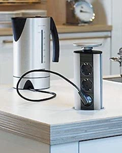 Torre de enchufes retráctil instalada en una encimera de cocina junto a un hervidor eléctrico